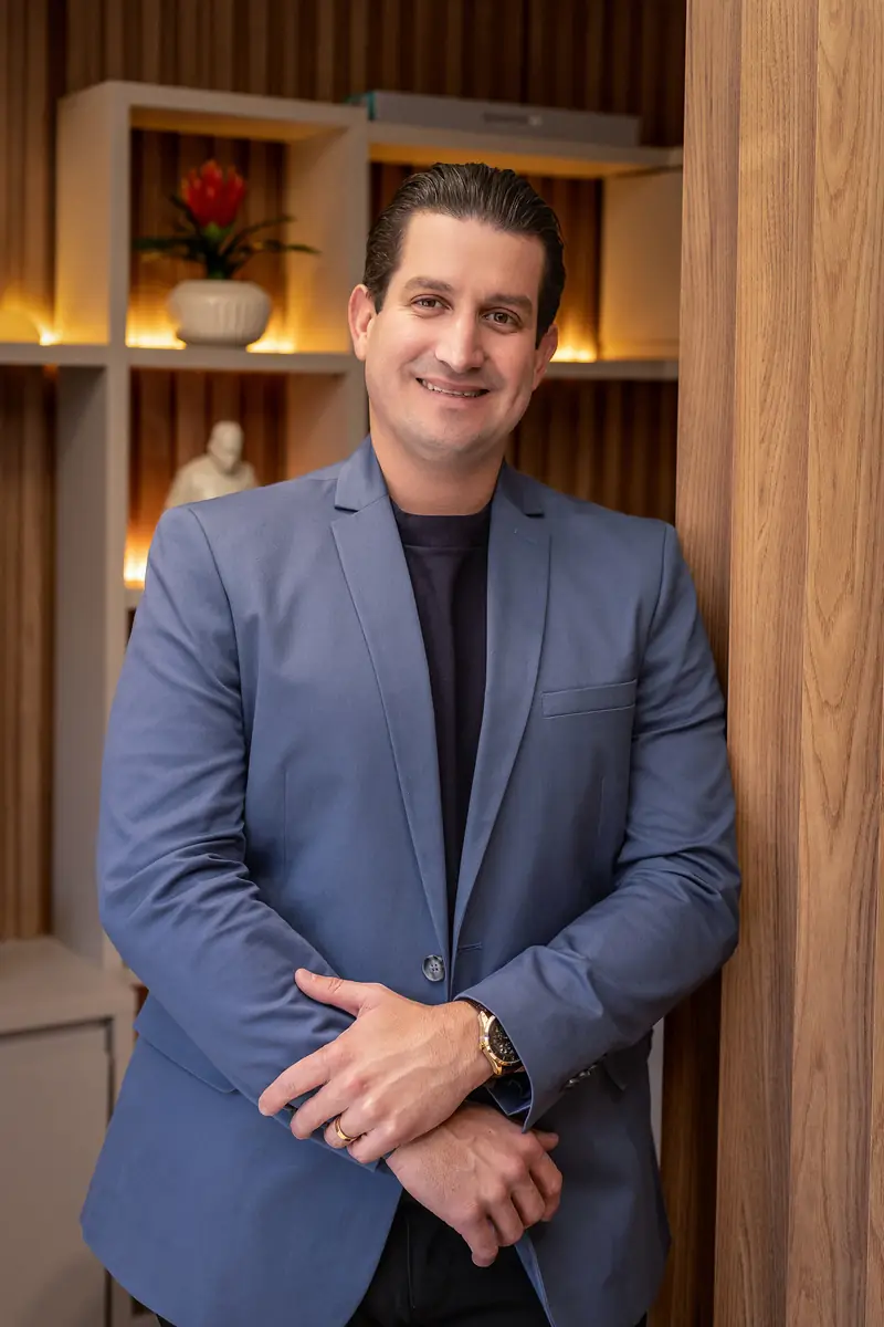 Dr. Felipe Seixas de blazer azul, em pé no consultório