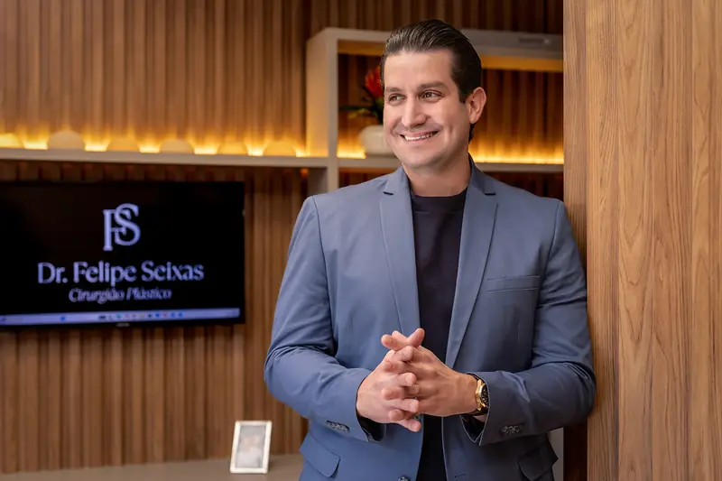 Dr. Felipe Seixas sorrindo ao lado do painel com o seu nome