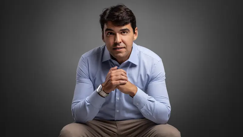 Médico psiquiatra de camisa azul sentado, em fundo cinza de estúdio