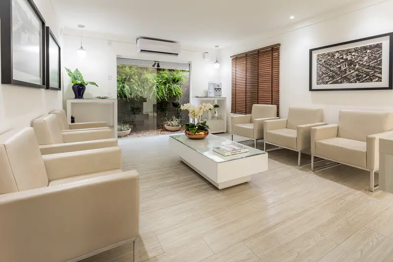 Recepção de clínica com poltronas claras e jardim interno