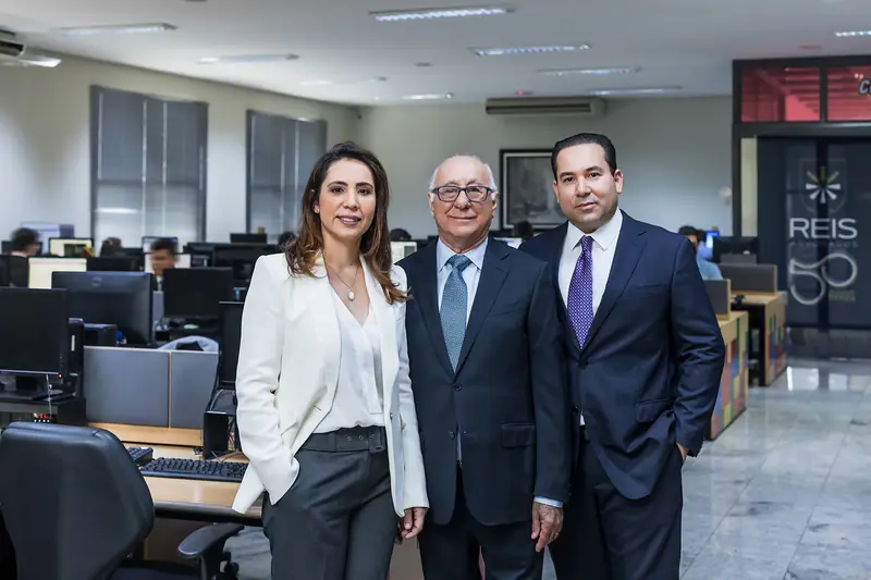 Três advogados em pé no salão de trabalho, com a equipe ao fundo