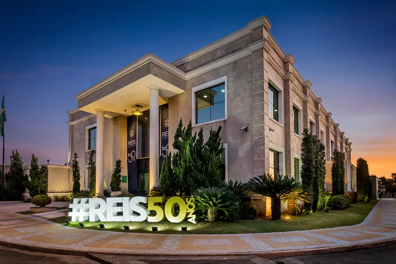 Sede do escritório ao entardecer, com o letreiro #REIS50 no jardim